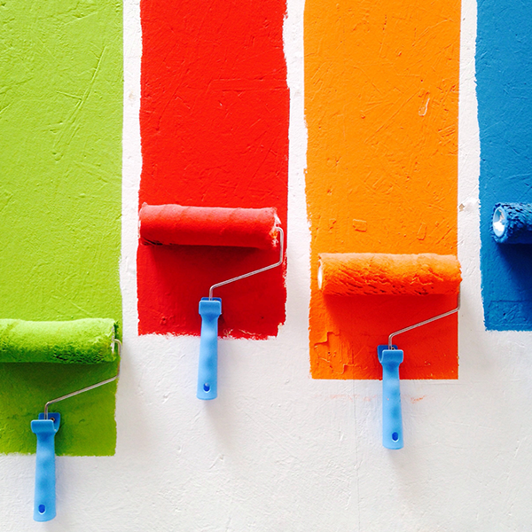 A red, green, orange, and blue paint roller being pulled down a white wall